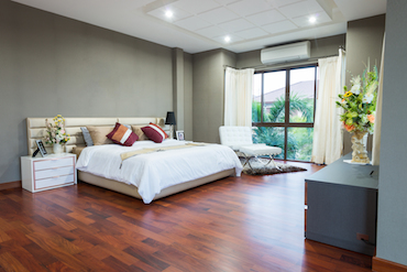 a large room with
               a hardwood floor, a tail window overlooking trees, a two-person bed with a
               single bedside table, and a padded chair next to the window